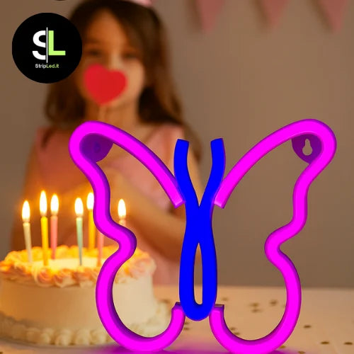 Insegna LED a forma di farfalla rosa e blu su un tavolo ad una festa di compleanno con logo StripLed.it