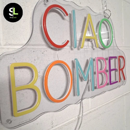 Insegna neon LED multicolor con scritta Ciao Bomber su plexiglass trasparente, vista da vicino in ambiente chiaro