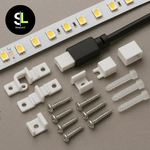 Set di accessori per strip LED composto da connettori supporti di fissaggio viti e tasselli posizionati accanto a una striscia LED SMD su sfondo grigio con logo StripLed.it