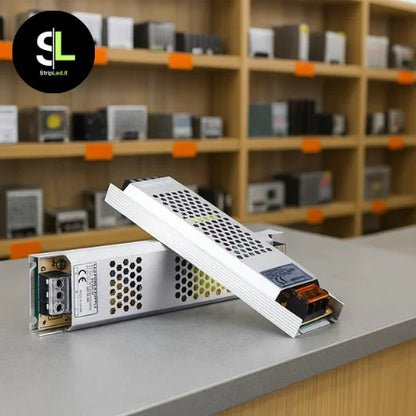 Alimentatore switching 24V ultrasottile mostrato in negozio con altri alimentatori professionali con logo StripLed.it