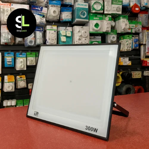 Faro LED 300W esposto su bancone di negozio con prodotti elettrici sullo sfondo e logo StripLed.it