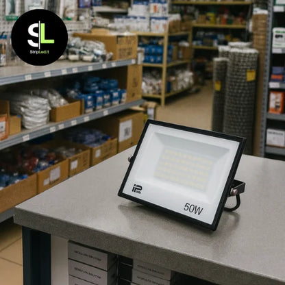 Faro LED 50W esposto su bancone di negozio con scaffali di prodotti elettrici sullo sfondo e logo StripLed.it