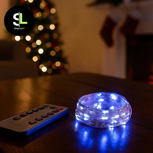 Filo di rame con luci LED bianco freddo acceso, sfondo natalizio con albero e luci soffuse con logo StripLed.it