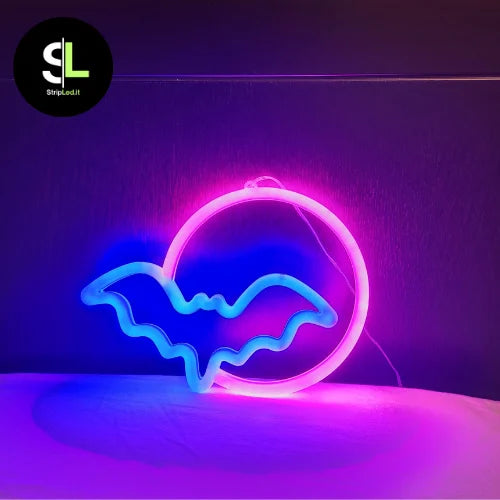 Insegna neon LED pipistrello con luce blu e rosa accesa su sfondo scuro e logo StripLed.it