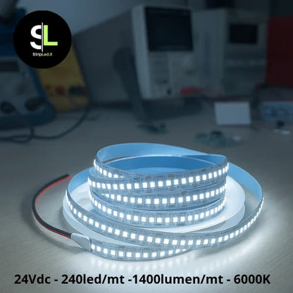 Striscia LED accesa su banco da lavoro con luce bianca fredda 6000K e strumenti elettronici sullo sfondo con logo StripLed.it