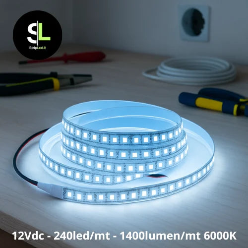 Striscia LED SMD 12V bianco freddo 6000K accesa su banco da lavoro e logo StripLed.it